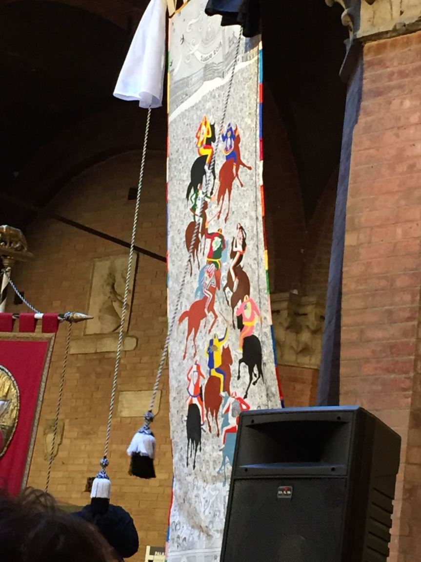 Palio di Siena: Da pochi minuti è stato svelato il Drappelone di Emilio&nbsp;Giannelli